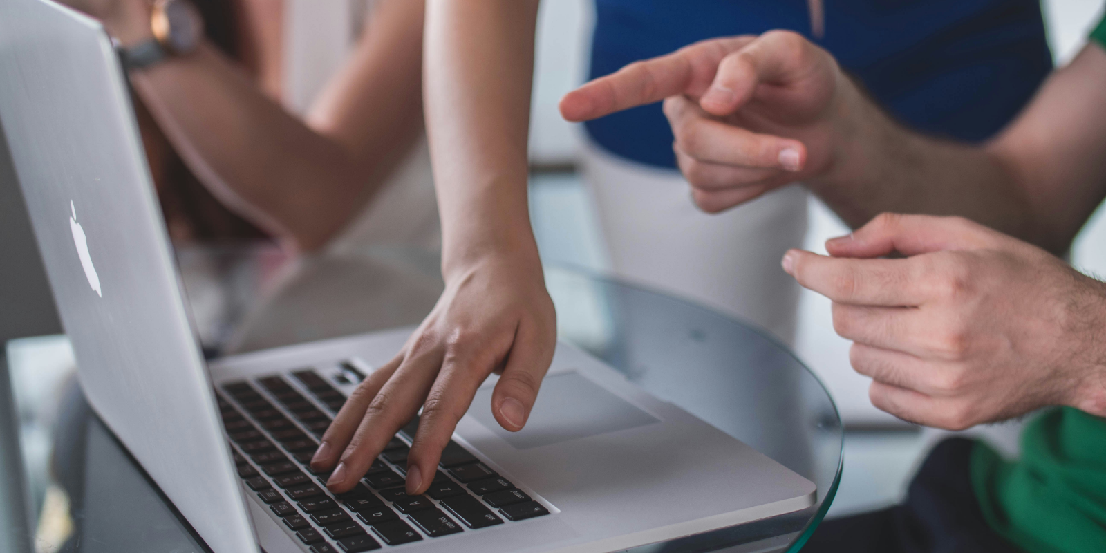 A photo showing people working together on a laptop. 