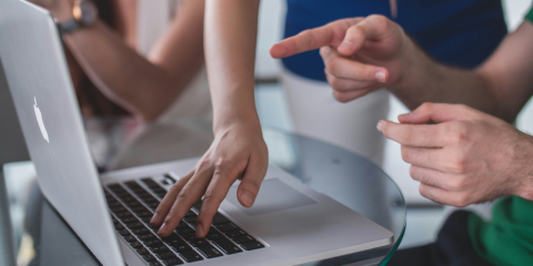 A photo showing people working together on a laptop. 